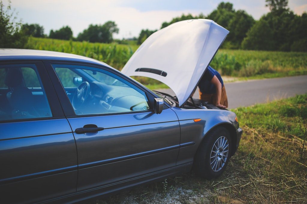 Man looking under the car hood trying to figure out if its the car battery or the starter