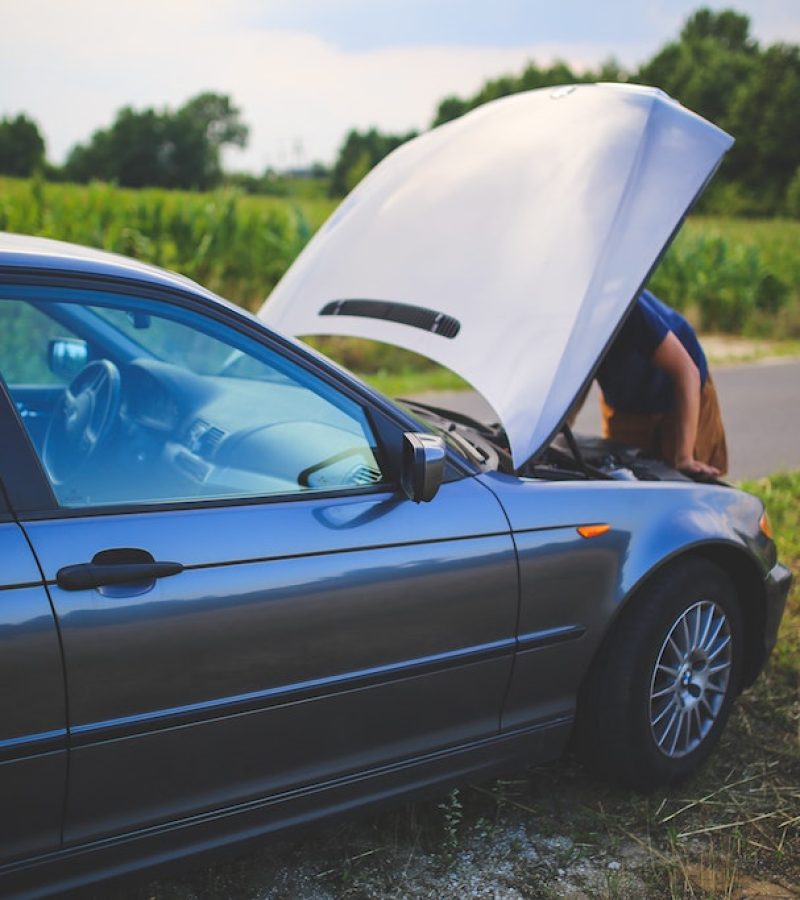 Man looking under the car hood trying to figure out if its the car battery or the starter